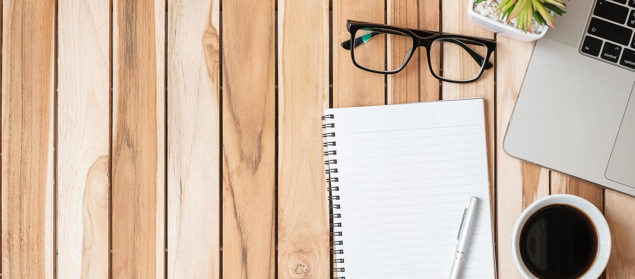 escritorio de oficina de vista superior con bolígrafo, computadora portátil, cuaderno en blanco, maceta y taza de café sobre fondo de mesa de madera. espacio de trabajo u oficina en casa con espacio de copia para el concepto de texto foto