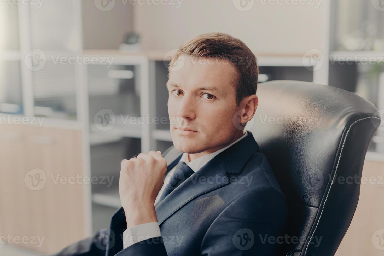 toma interior de un hombre de negocios serio y confiado posa en la silla, posa en el gabinete, espera a que los colegas discutan los principales temas de trabajo. joven director masculino en traje formal, piensa en un nuevo proyecto foto
