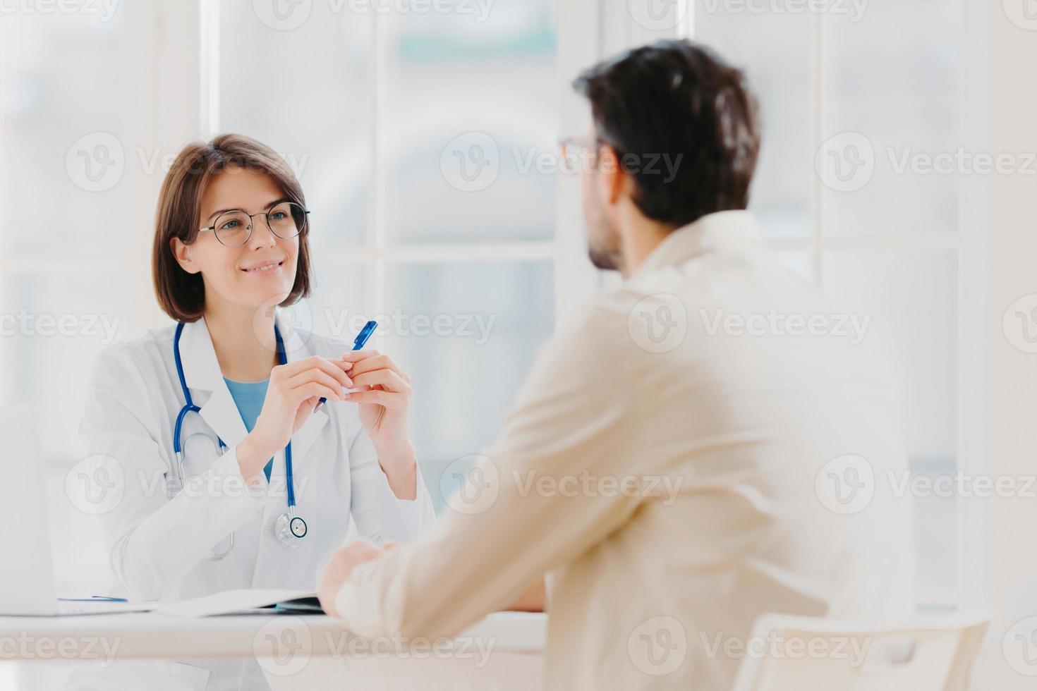 Heath care and medical consultancy concept. Skilled therapist in white uniform talks with patient, writes down in medical history, listens attentively all symptoms, tries to prevent serious disease photo