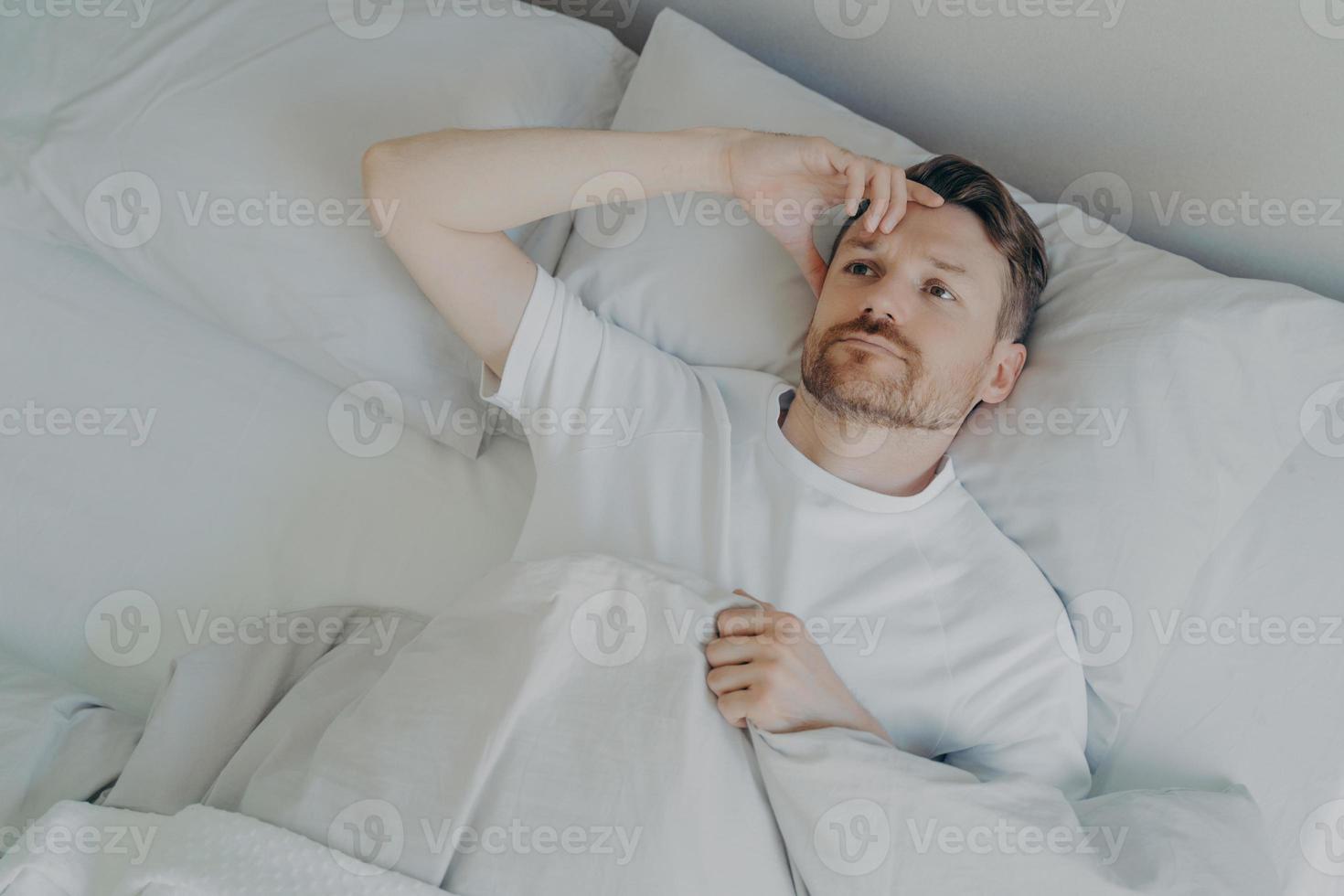 Young tired bearded man lying on bed with open eyes photo