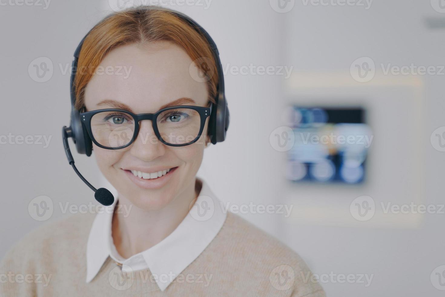 Young lady consultant of call center. European friendly girl in headset talking to client in agency. photo