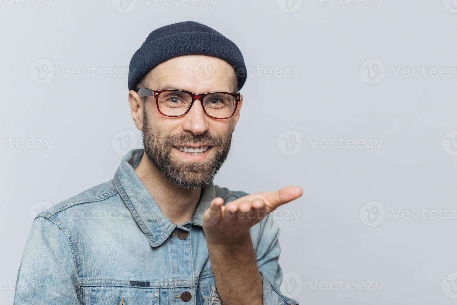 un hombre alegre con barba y gafas de moda expresa su amor, muestra un beso al aire, tiene una expresión alegre, aislado sobre un fondo gris. hombre de mediana edad de ojos azules con ropa elegante, gestos interiores foto