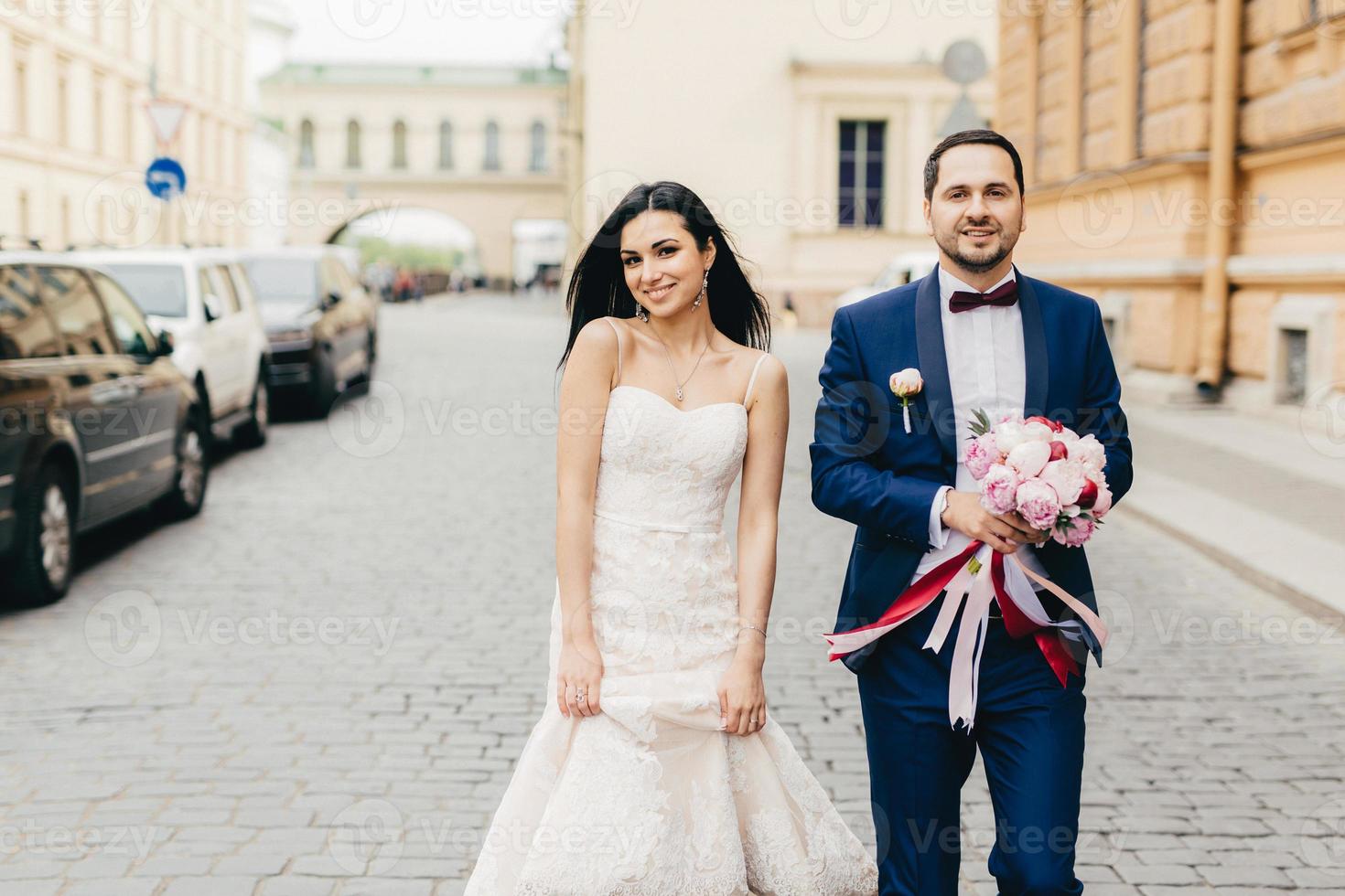el novio y la novia caminan juntos, posan ante la cámara, tienen expresiones complacidas, celebran su boda, son fotografiados para el álbum familiar. romántica pareja joven feliz tiene un día especial. foto