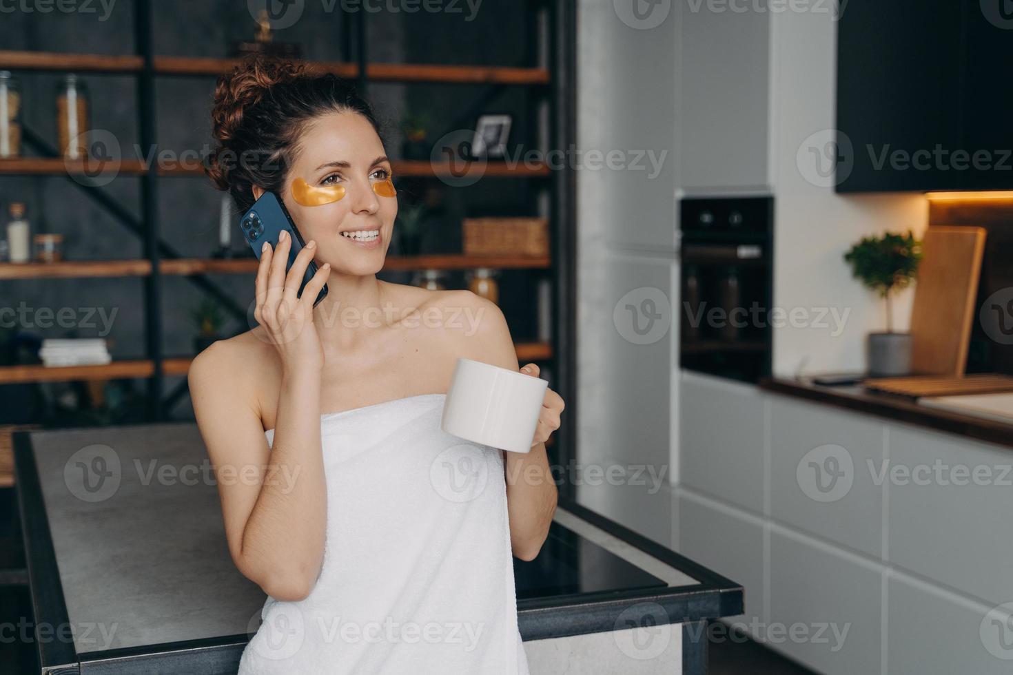 Weekend morning phone talk. Young woman applies anti wrinkle eye patches and talking on phone. photo