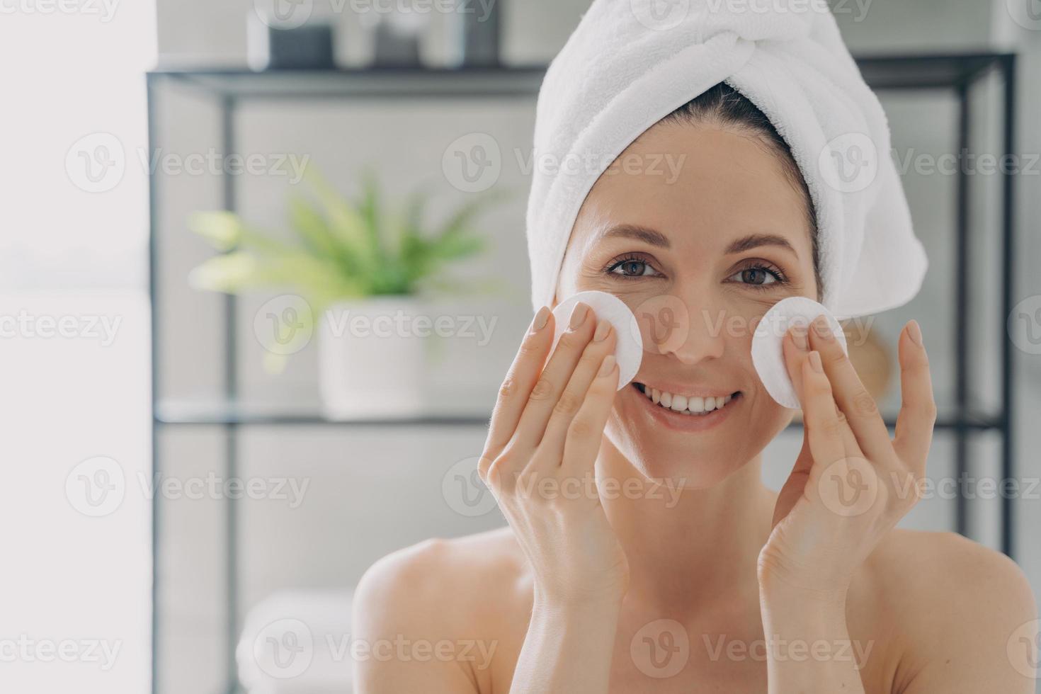 Girl is cleansing skin with face toner and cotton disks. Attractive young woman after bathing. photo