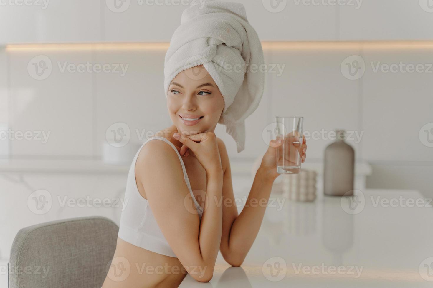 Side portrait of beautiful caucasian female sitting in kitchen with glass of water photo