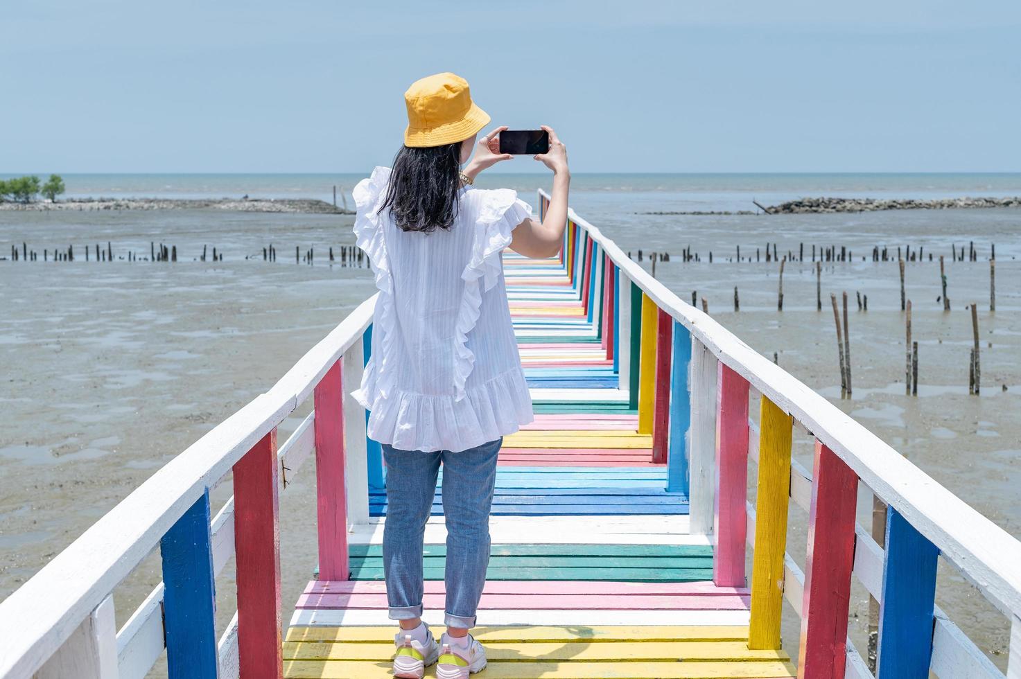 la vista trasera de una mujer asiática de pie y tomando una foto en el puente del arco iris para ver el punto de vista en la provincia de samut sakorn.