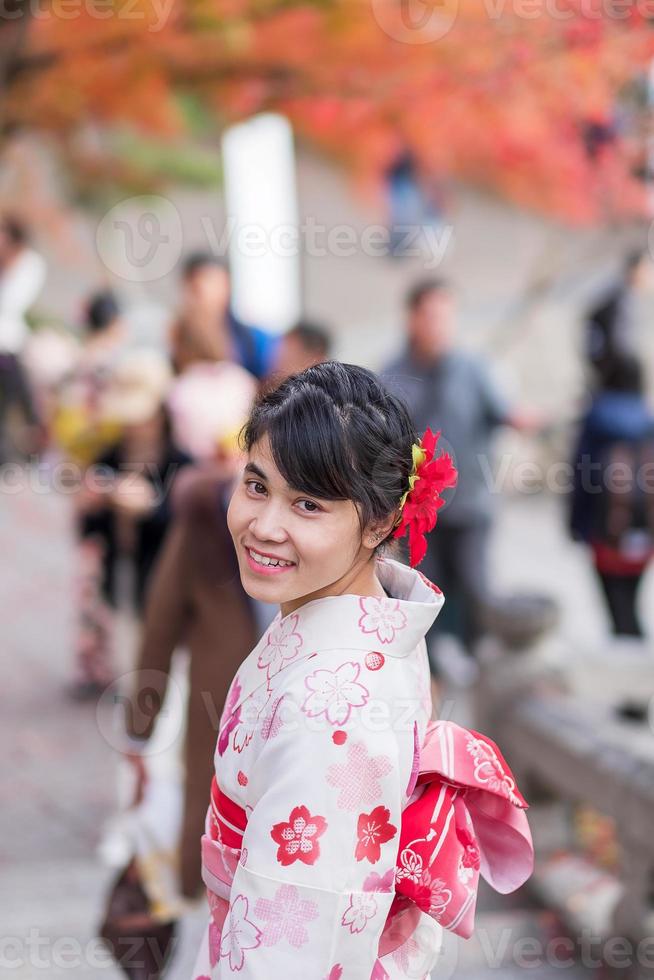 joven turista vistiendo kimono disfrutando con hojas coloridas en el templo kiyomizu dera, kyoto, japón. chica asiática con estilo de cabello en ropa tradicional japonesa en la temporada de follaje de otoño foto