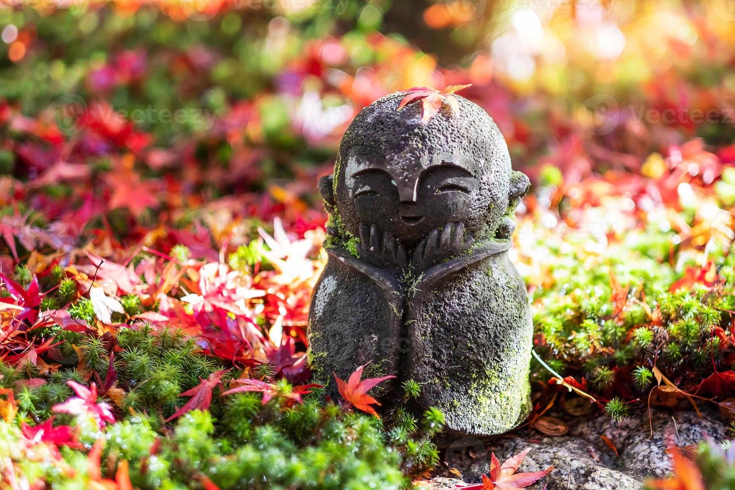 Japanese Jizo sculpture doll with falling Red Maple leaf in Japanese Garden at Enkoji Temple, Kyoto, Japan. Landmark and famous in Autumn season photo