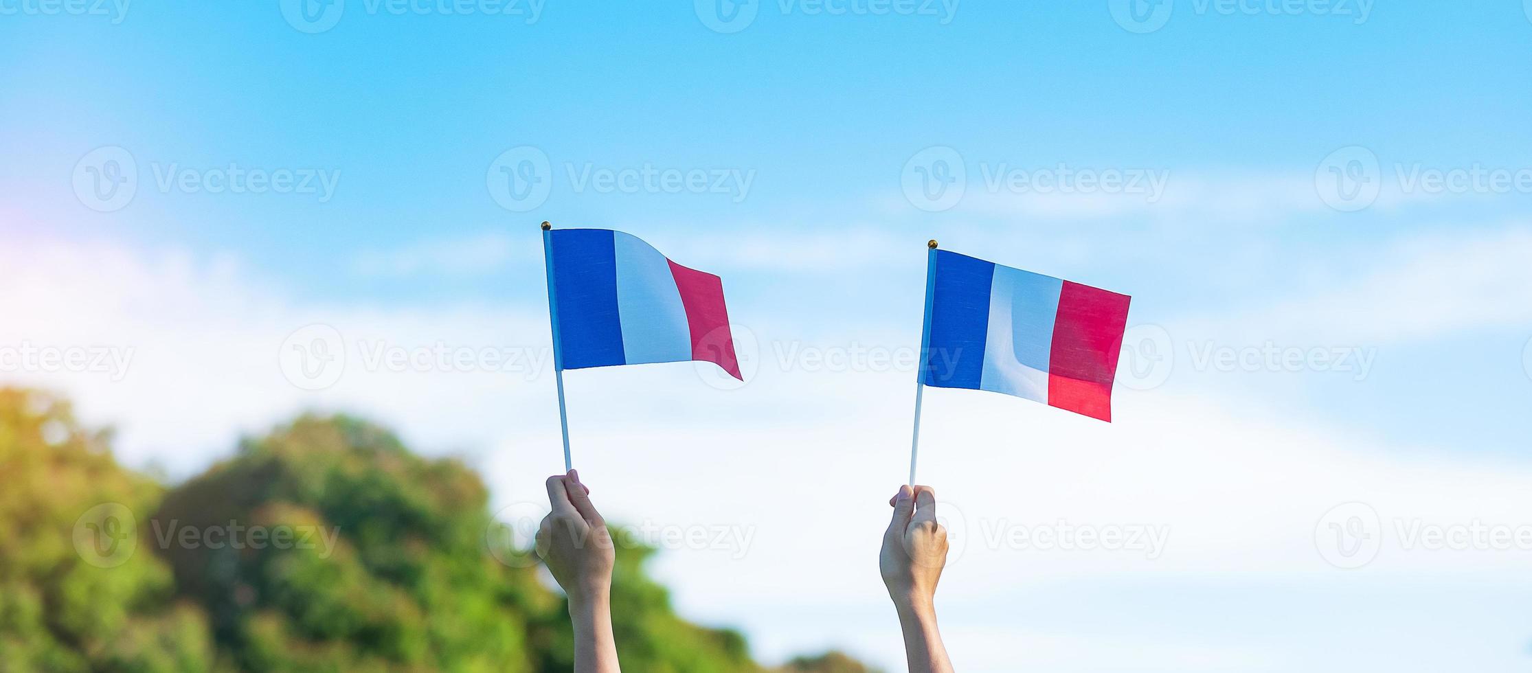 mano que sostiene la bandera de Francia sobre fondo de cielo azul. fiesta del día nacional francés, día de la bastilla y conceptos de celebración feliz foto