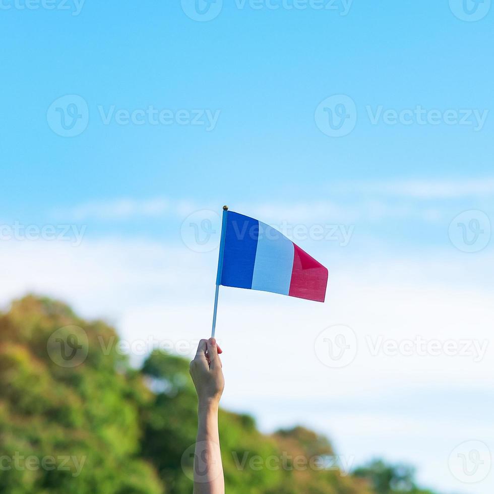 mano que sostiene la bandera de Francia sobre fondo de cielo azul. fiesta del día nacional francés, día de la bastilla y conceptos de celebración feliz foto