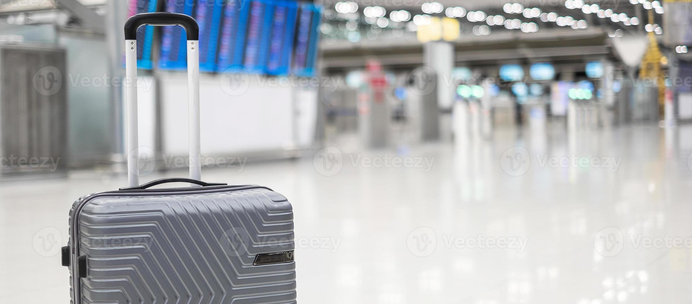 luggage bag in international airport terminal, trolley suitcase with information board in aerodrome background. Transport, insurance, travel and vacation concepts photo