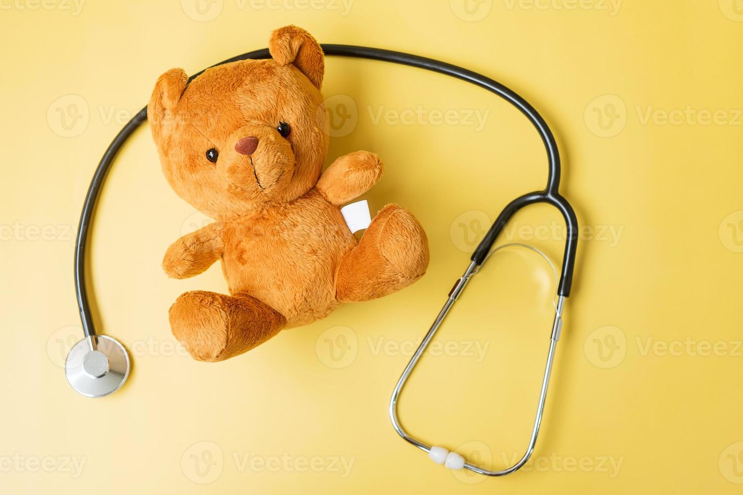 estetoscopio con muñeca de oso sobre fondo amarillo para apoyar la vida y la enfermedad de los niños. mes de concientización sobre el cáncer infantil de septiembre, concepto de seguro de vida y atención médica foto