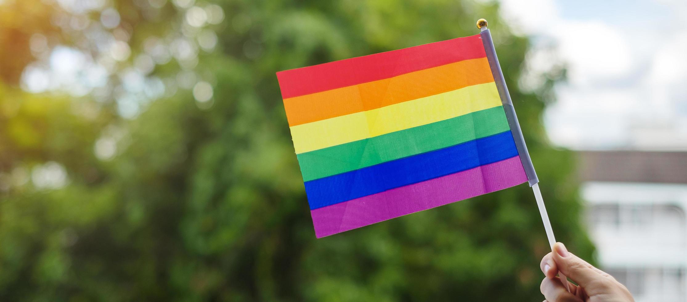 hands showing LGBTQ Rainbow flag on green nature background. Support Lesbian, Gay, Bisexual, Transgender and Queer community and Pride month concept photo