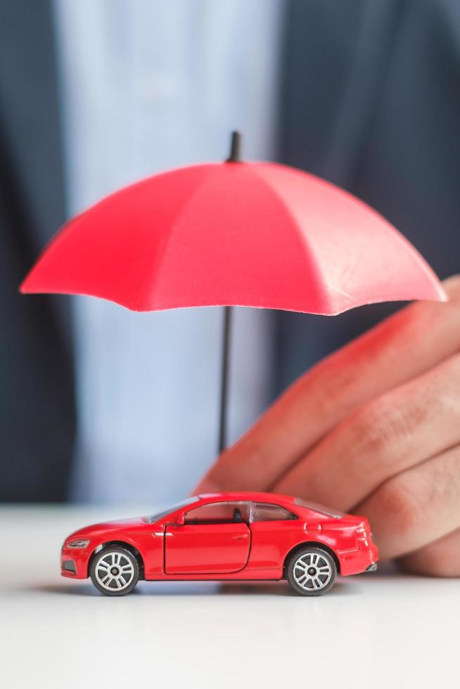 Businessman hand holding umbrella and cover  red car toy on table. Car insurance, warranty, repair, Financial, banking and money concept photo