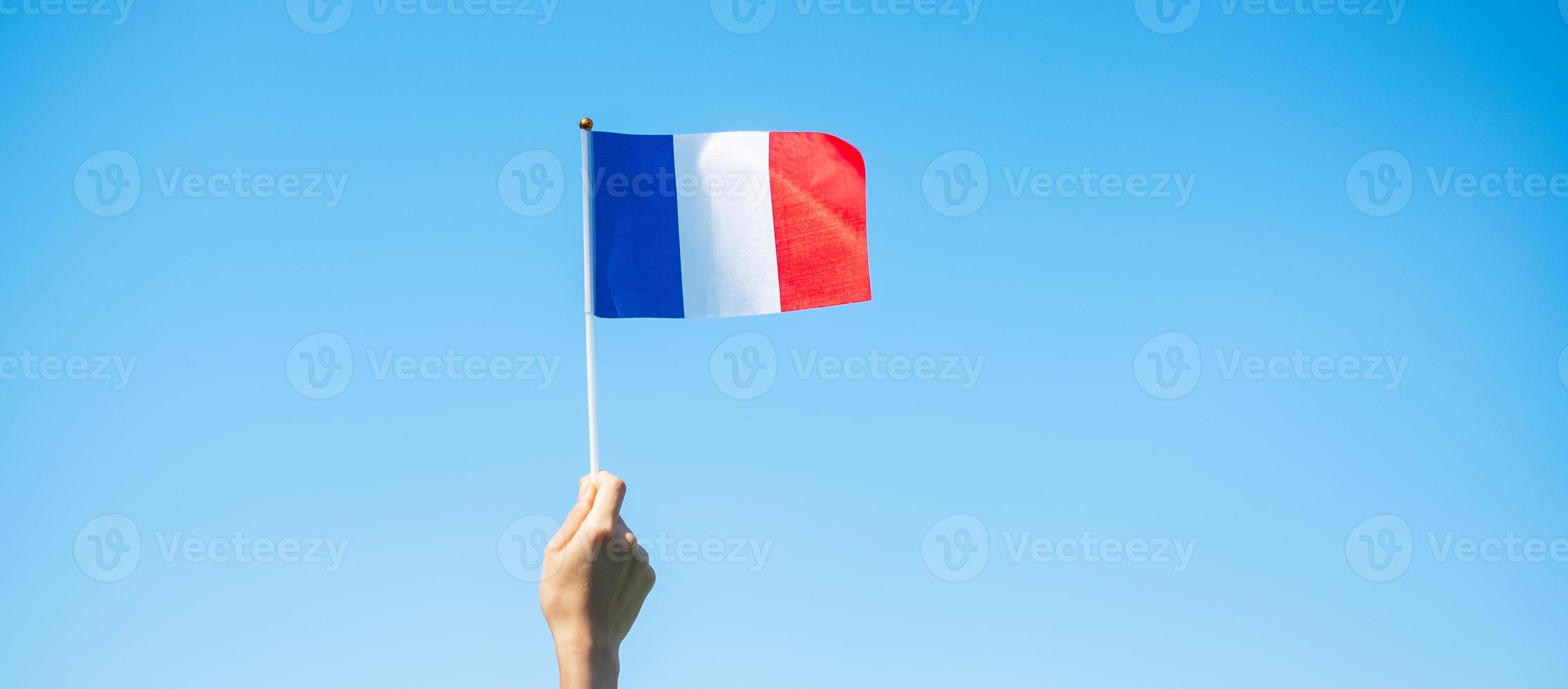 mano que sostiene la bandera de Francia sobre fondo de cielo azul. fiesta del día nacional francés, día de la bastilla y conceptos de celebración feliz foto