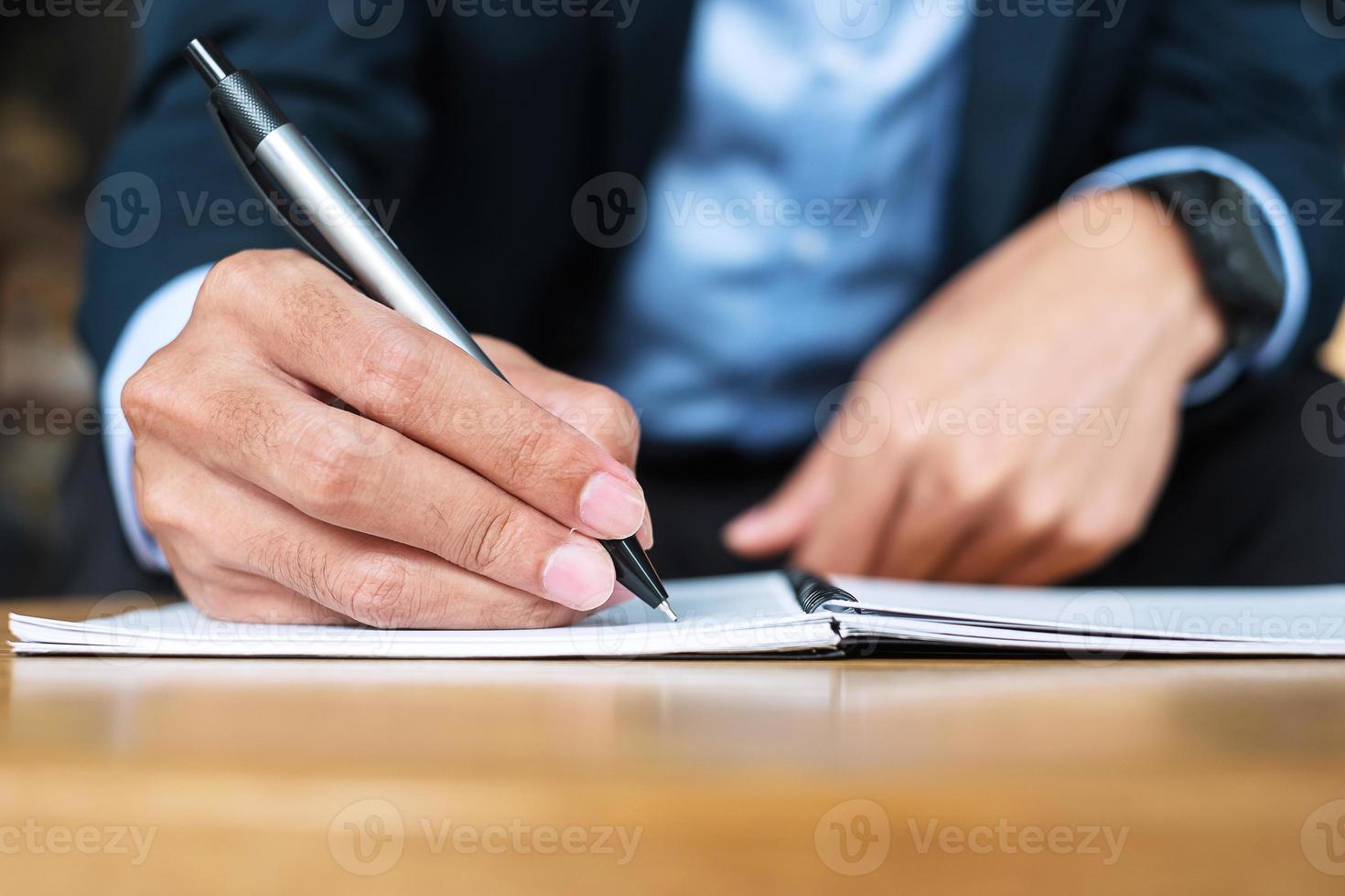 Businessman in suit writing something on notebook in office or cafe, hand of man holding pen with signature on paper report. business concepts photo