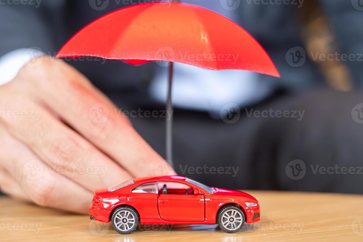 mano de hombre de negocios sosteniendo la cubierta del paraguas o el juguete del coche rojo de protección en la mesa. concepto financiero, de dinero, de refinanciamiento y de seguro de automóvil foto