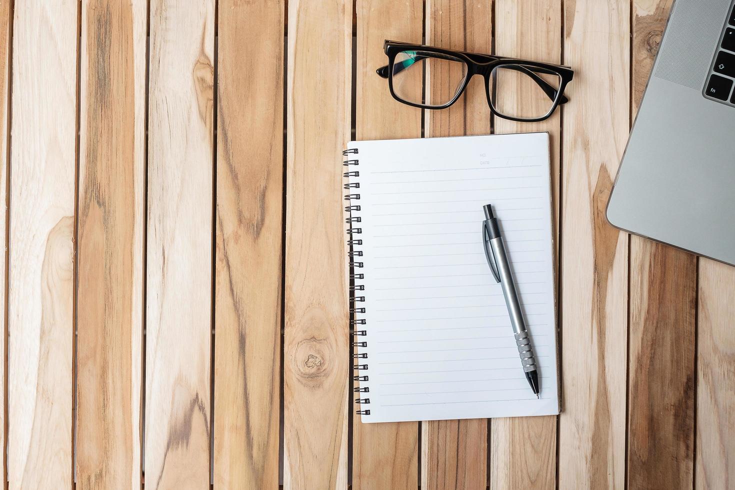 escritorio de oficina de vista superior con bolígrafo, computadora portátil y cuaderno en blanco sobre fondo de mesa de madera. espacio de trabajo u oficina en casa con espacio de copia para el concepto de texto foto