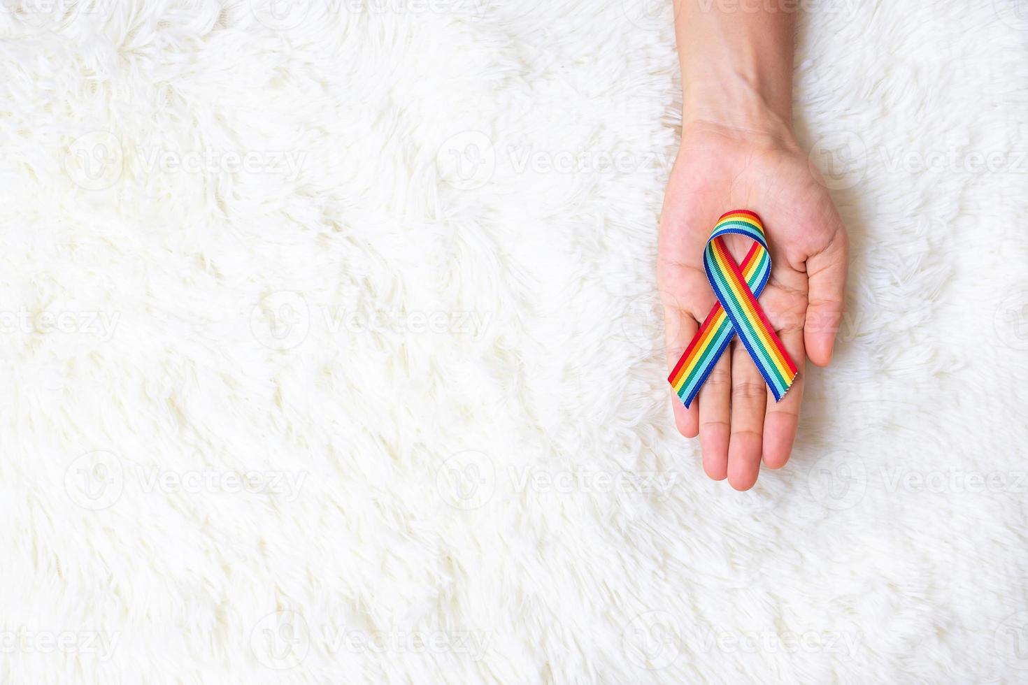 hand showing LGBTQ Rainbow ribbon on white bed background. Support Lesbian, Gay, Bisexual, Transgender, Queer community and Rights concept photo