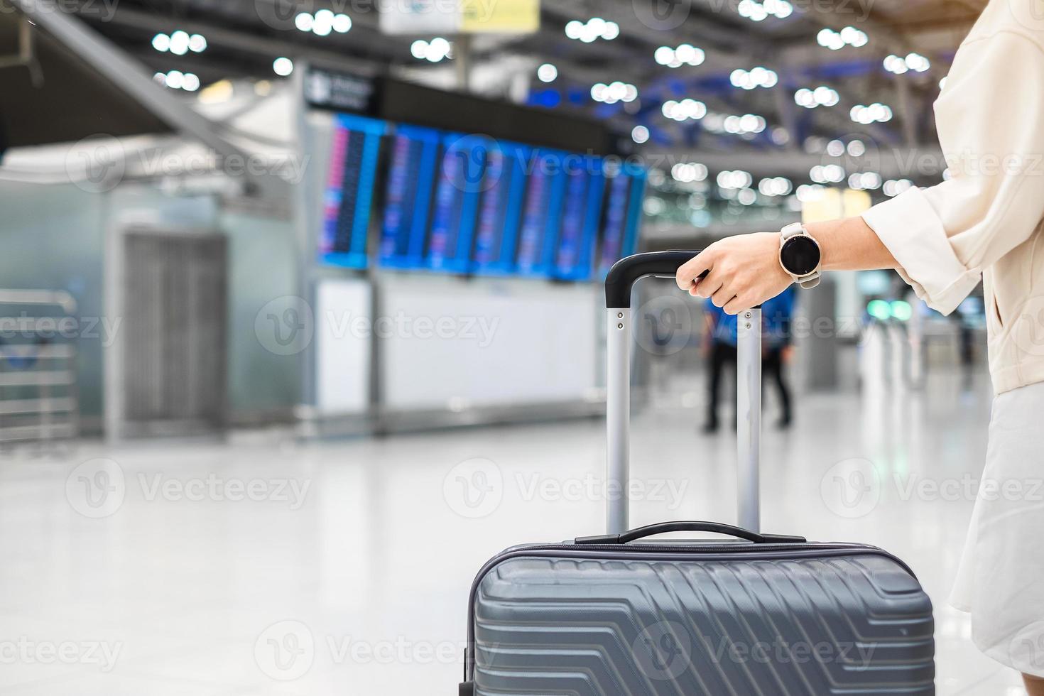 Young woman hand holding luggage handle before checking flight time in airport, Transport, insurance, travel and vacation concepts photo