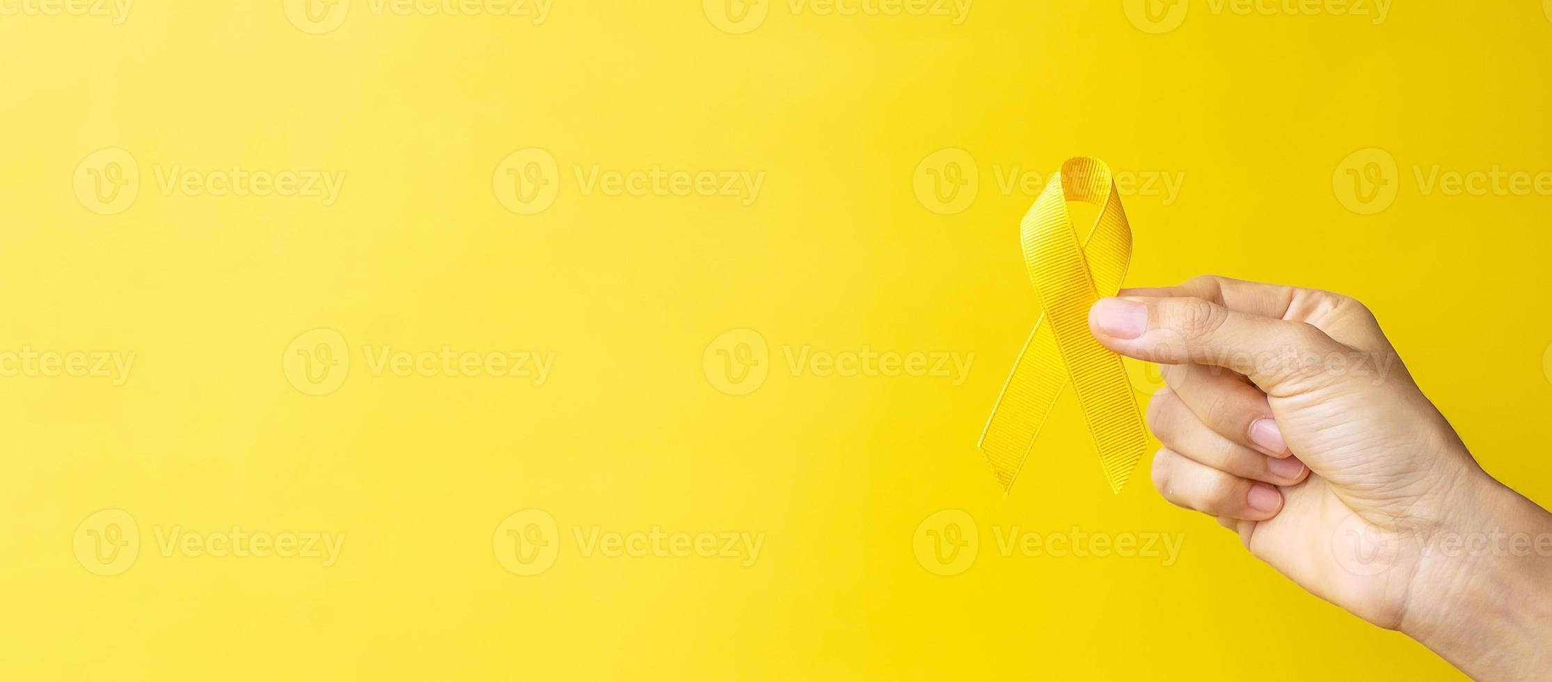 hand showing Yellow Ribbon on yellow background for supporting people living and illness. September Suicide prevention day, Childhood Cancer Awareness month and World cancer day concept photo