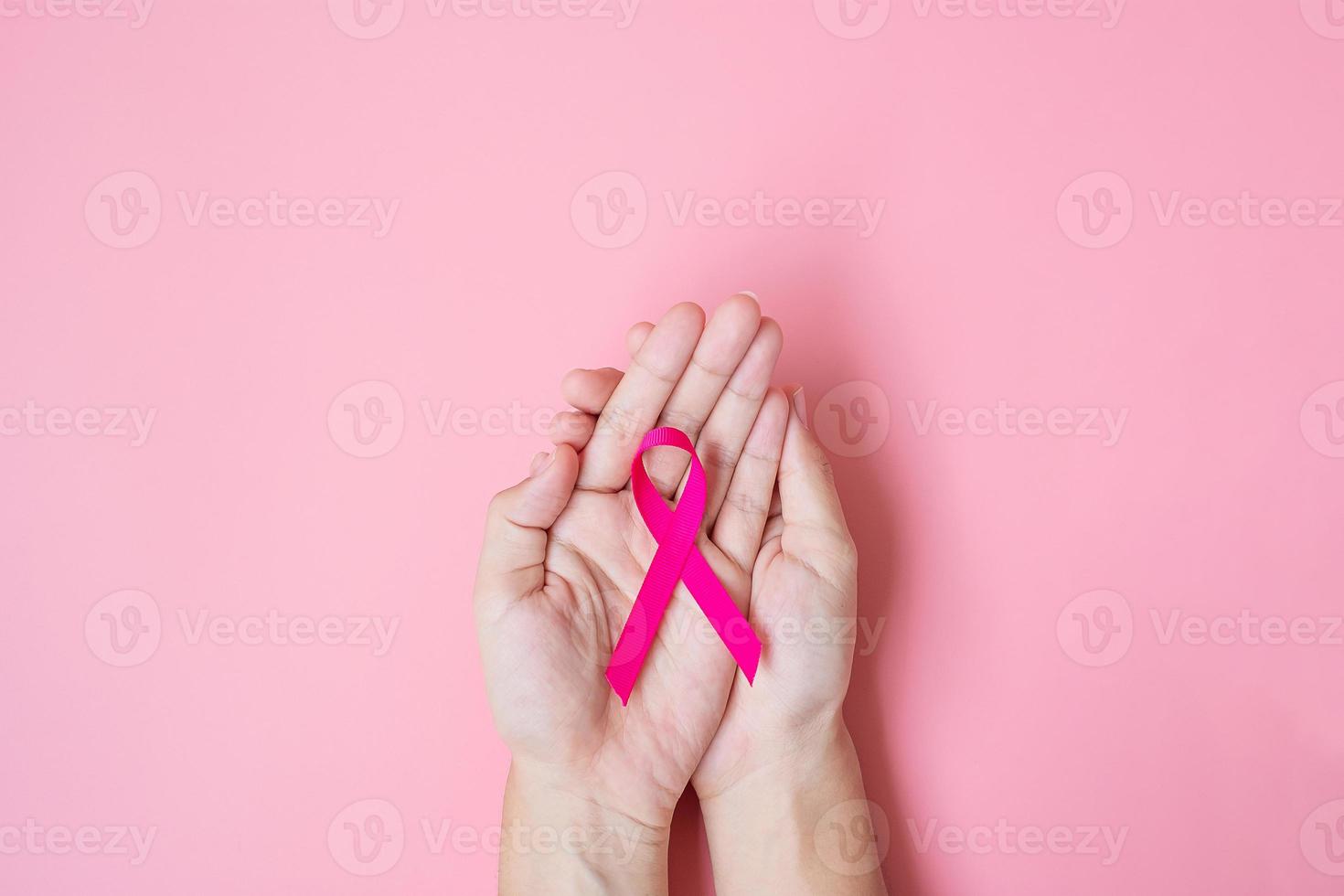 octubre mes de concientización sobre el cáncer de mama, mano de mujer adulta sosteniendo una cinta rosa sobre fondo rosa para apoyar a las personas que viven y están enfermas. concepto del día internacional de la mujer, la madre y el día mundial del cáncer foto