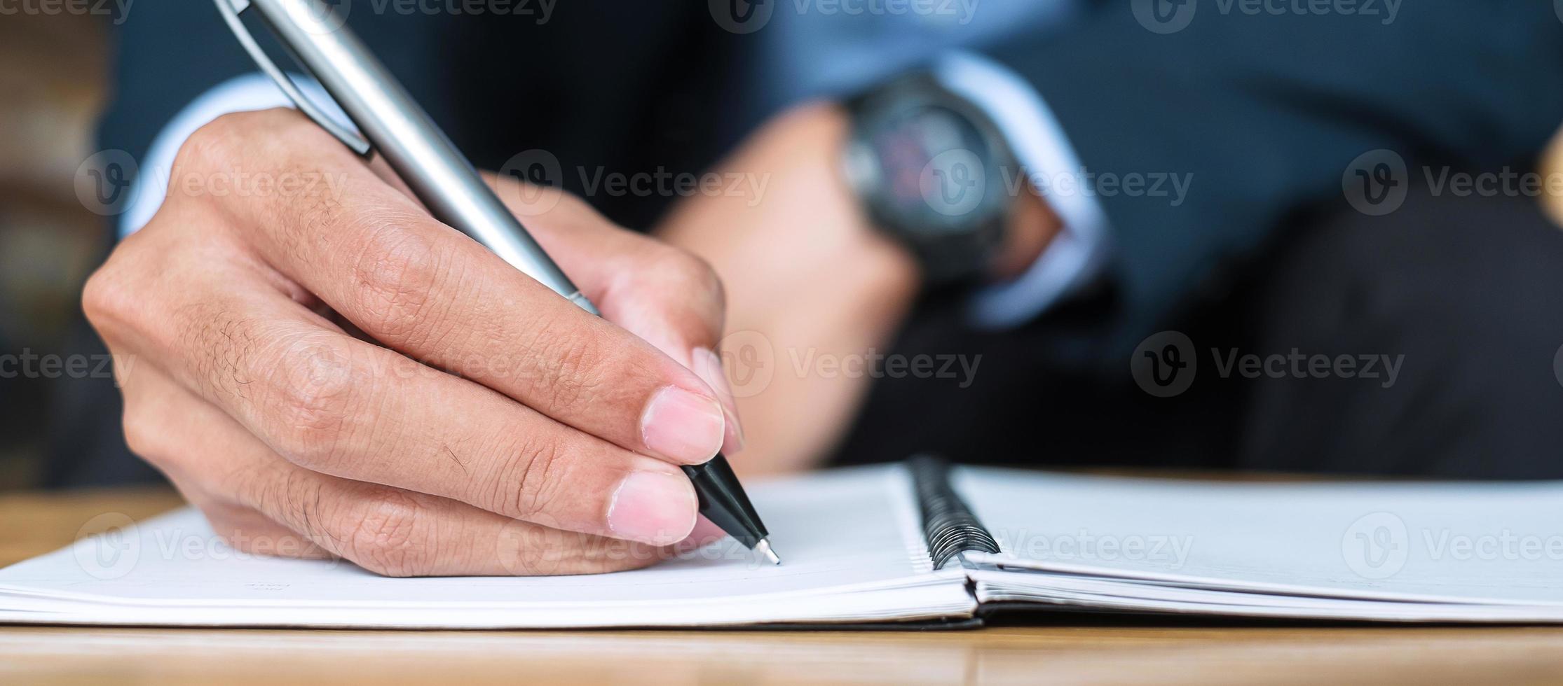 Businessman in suit writing something on notebook in office or cafe, hand of man holding pen with signature on paper report. business concepts photo