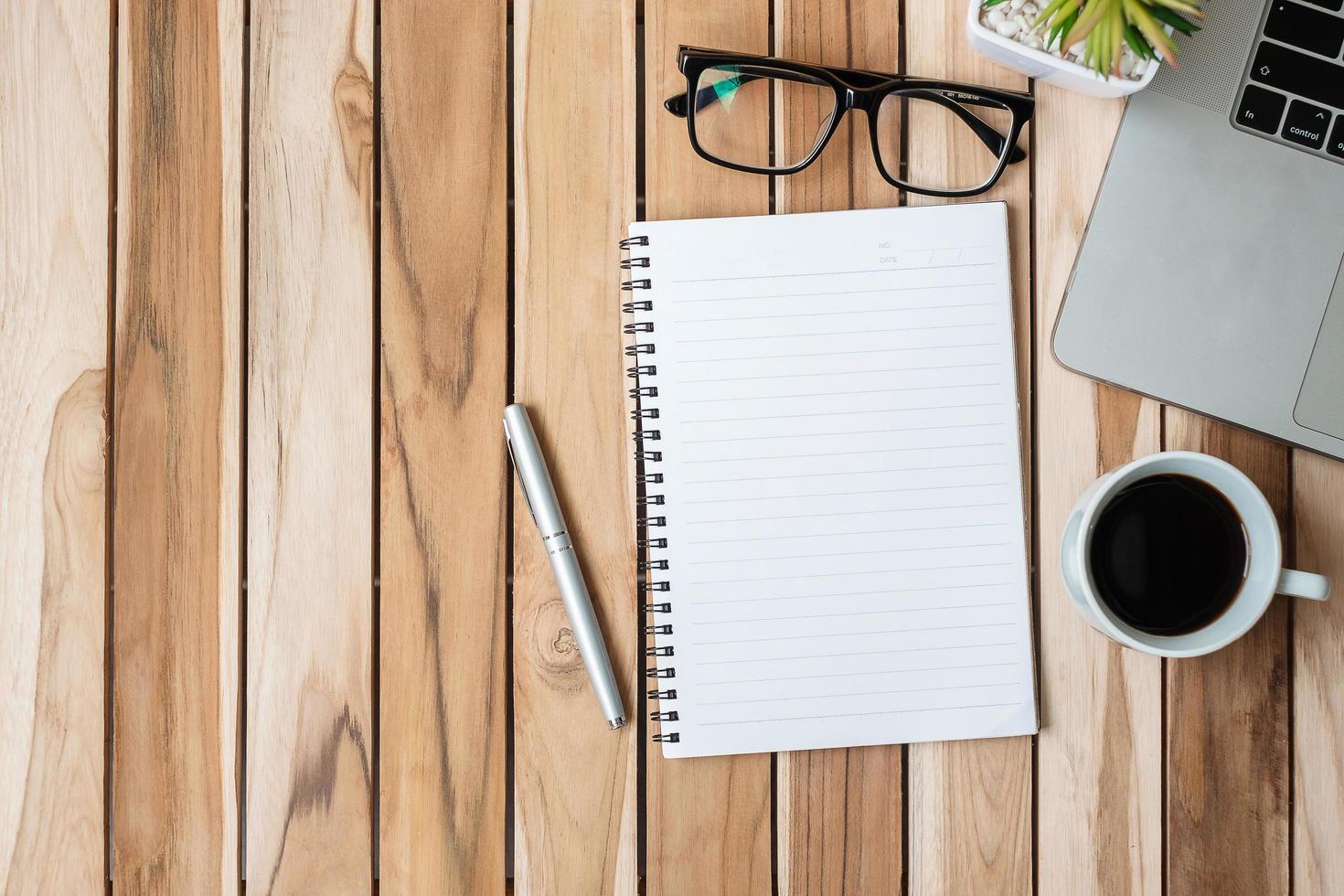 escritorio de oficina de vista superior con bolígrafo, computadora portátil, cuaderno en blanco, maceta y taza de café sobre fondo de mesa de madera. espacio de trabajo u oficina en casa con espacio de copia para el concepto de texto foto