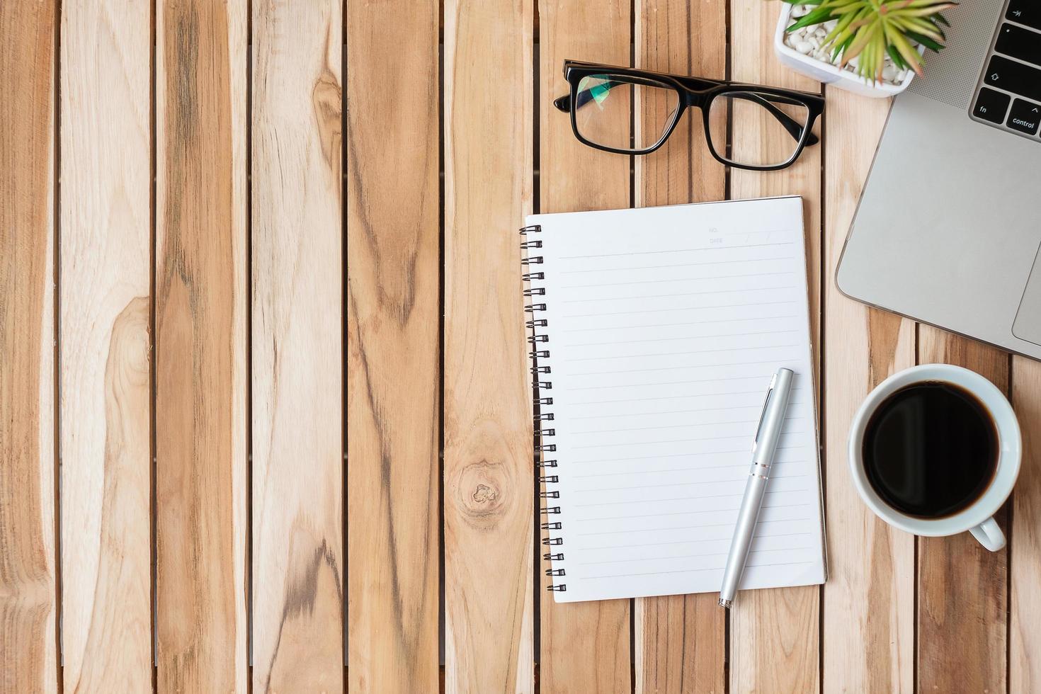 escritorio de oficina de vista superior con bolígrafo, computadora portátil, cuaderno en blanco, maceta y taza de café sobre fondo de mesa de madera. espacio de trabajo u oficina en casa con espacio de copia para el concepto de texto foto