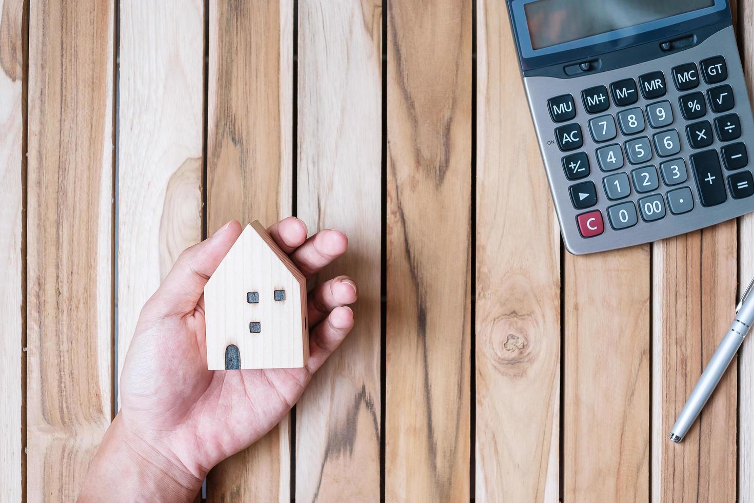 Hand holding house model with calculator and pen on wooden background. Financial, money, refinance, Real estate and new home concept photo