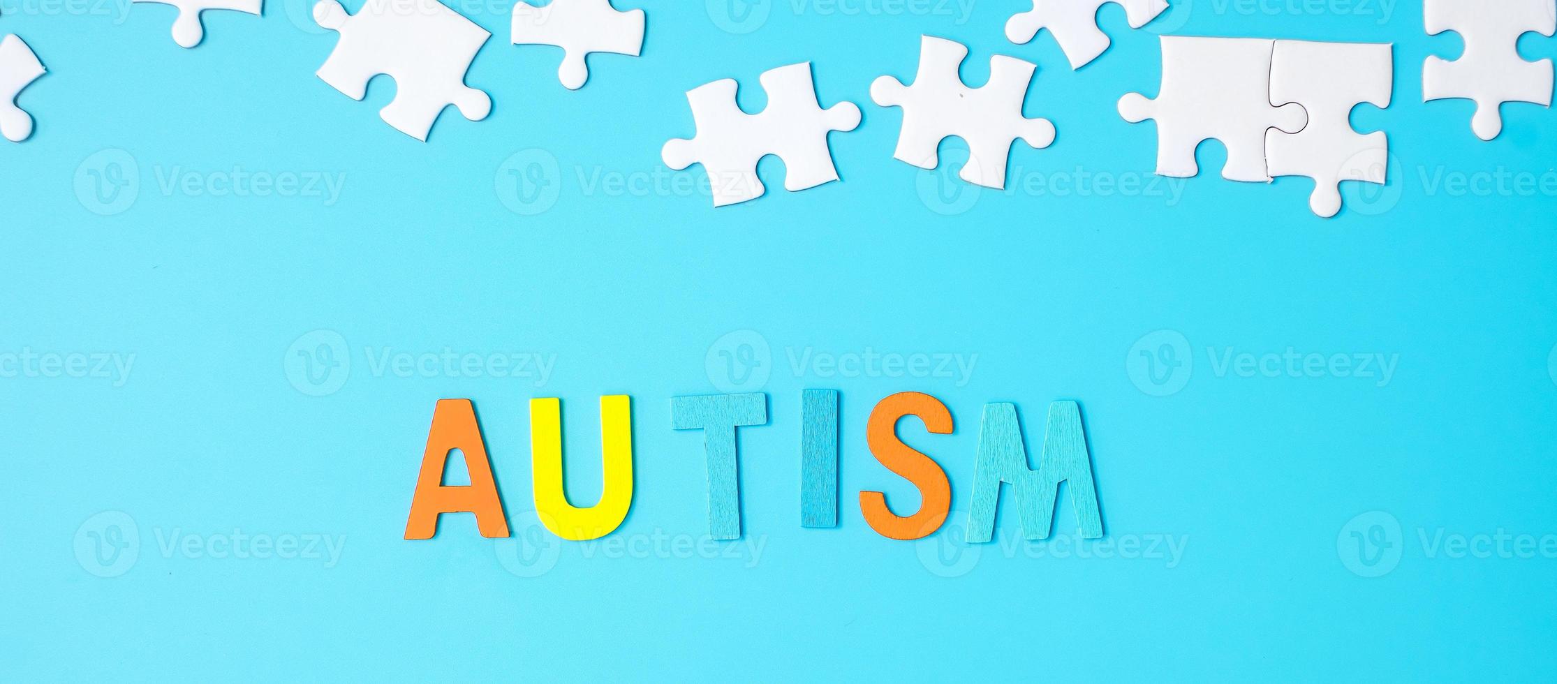 texto de autismo con piezas de rompecabezas blancas sobre fondo azul. conceptos de salud, trastorno del espectro autista y día mundial de concienciación sobre el autismo foto
