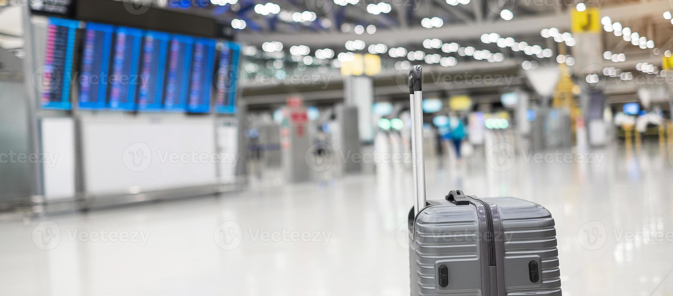 luggage bag in international airport terminal, trolley suitcase with information board in aerodrome background. Transport, insurance, travel and vacation concepts photo