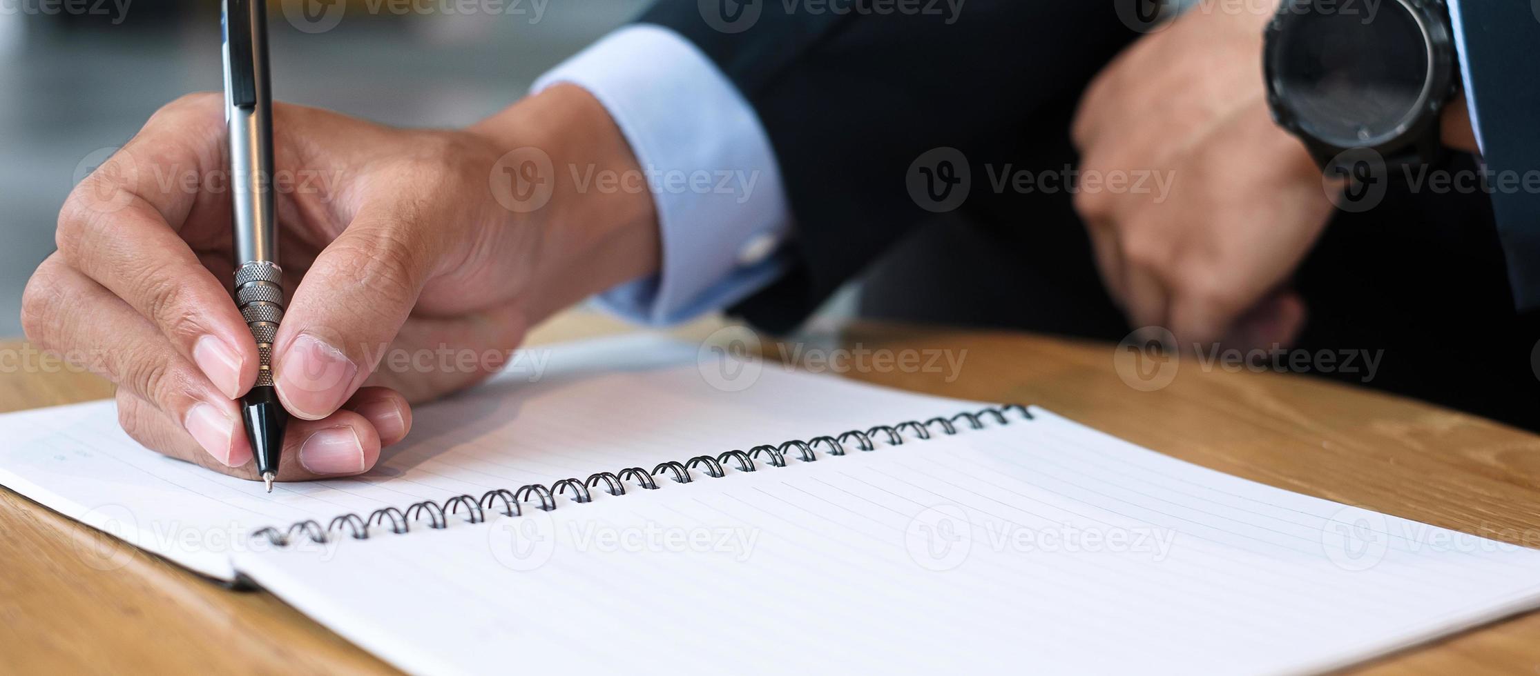 Businessman in suit writing something on notebook in office or cafe, hand of man holding pen with signature on paper report. business concepts photo
