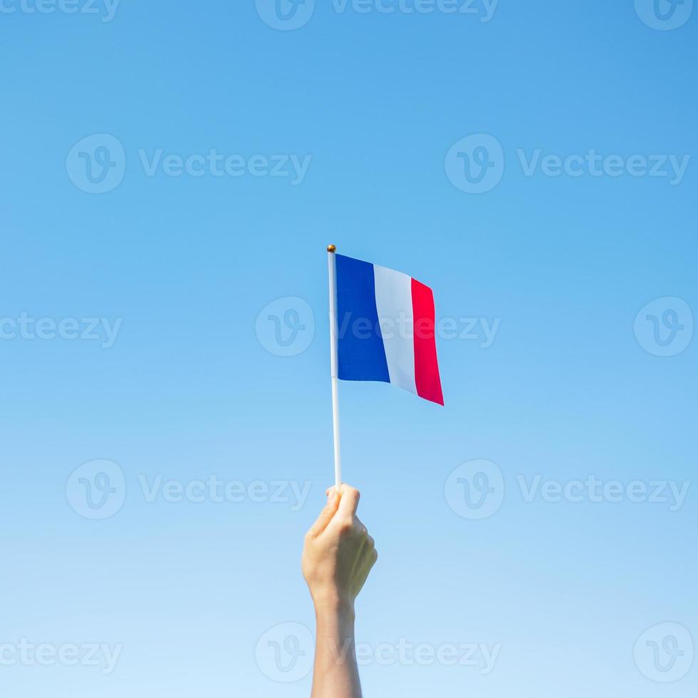 mano que sostiene la bandera de Francia sobre fondo de cielo azul. fiesta del día nacional francés, día de la bastilla y conceptos de celebración feliz foto