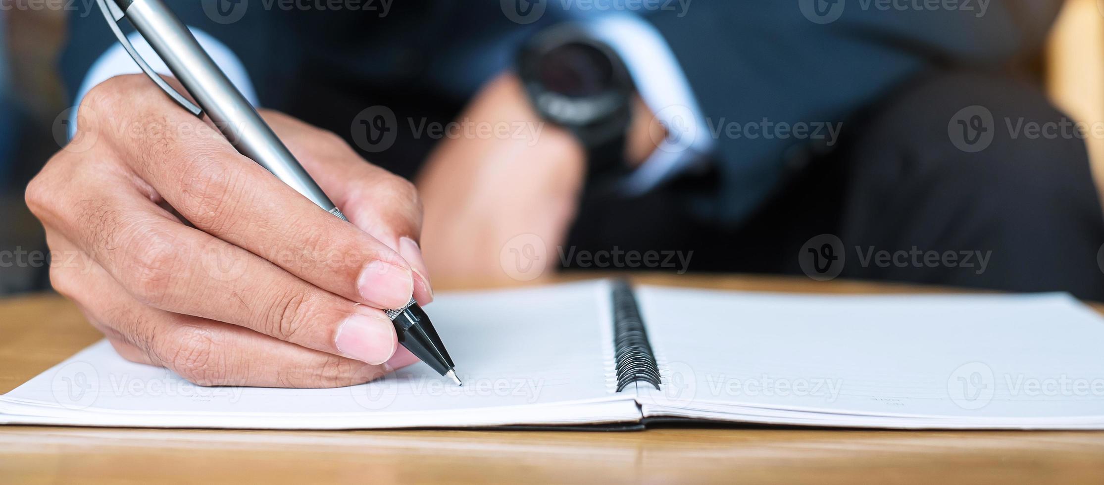 Businessman in suit writing something on notebook in office or cafe, hand of man holding pen with signature on paper report. business concepts photo