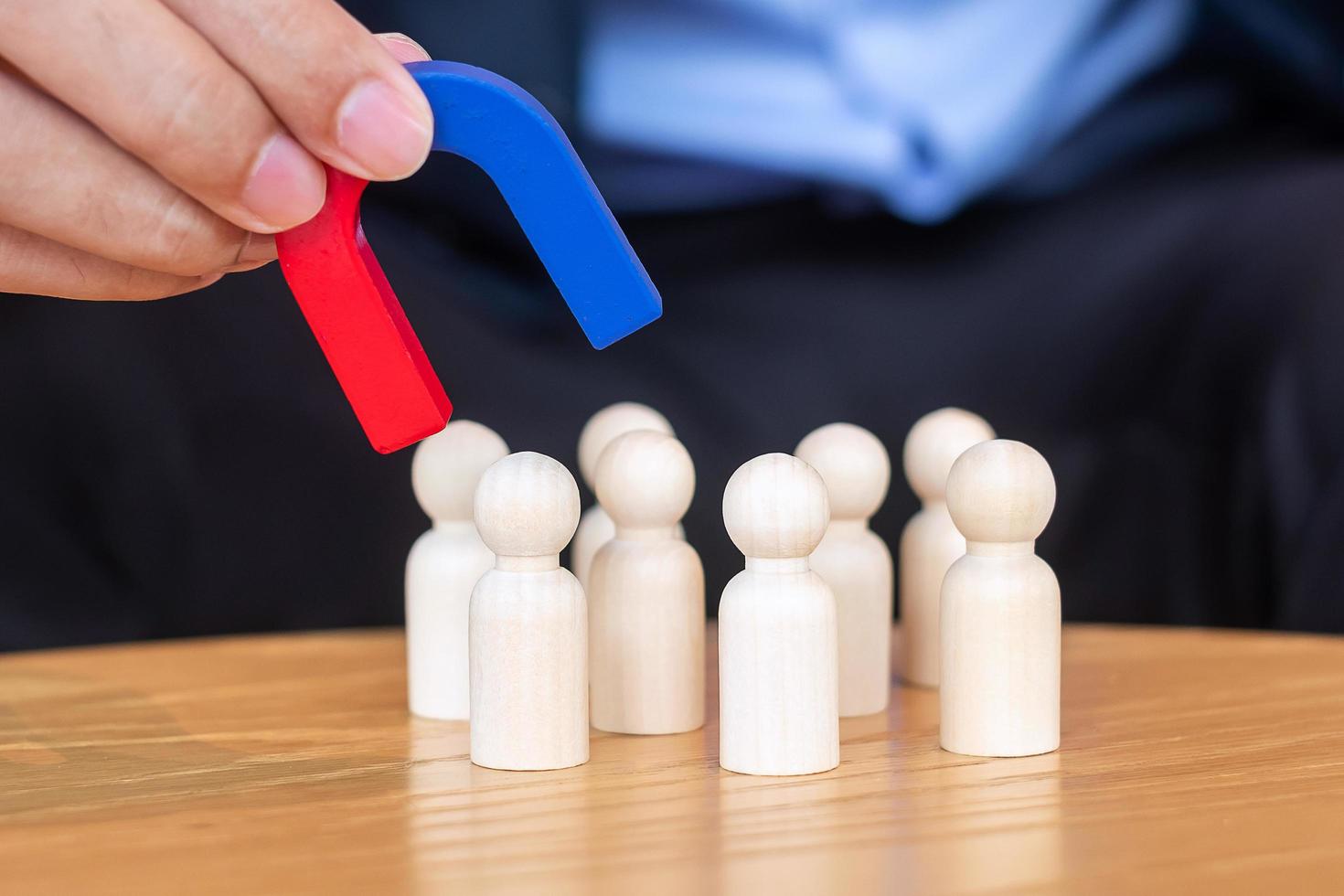 mano de hombre de negocios sosteniendo un imán y tirando de la figura de madera del hombre del empleado de la multitud. negocios, gestión de recursos humanos, reclutamiento, trabajo en equipo, estrategia, personas tóxicas y conceptos de liderazgo foto