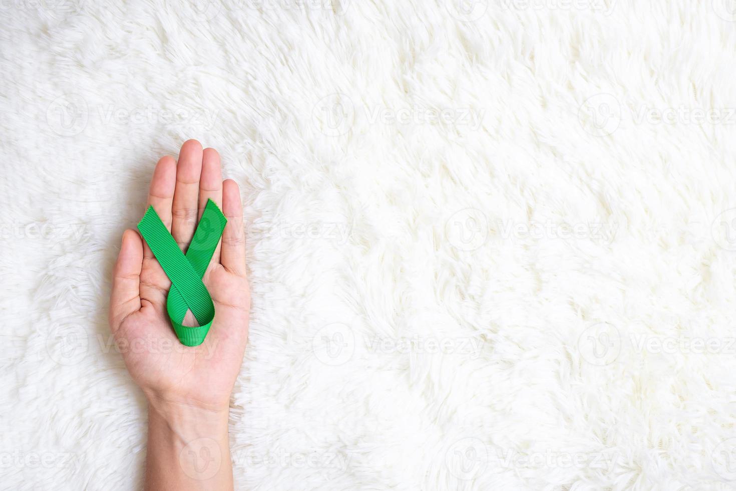 Hand holding green Ribbon for supporting people living and illness. Liver, Gallbladders bile duct, kidney Cancer and Lymphoma Awareness month concept photo