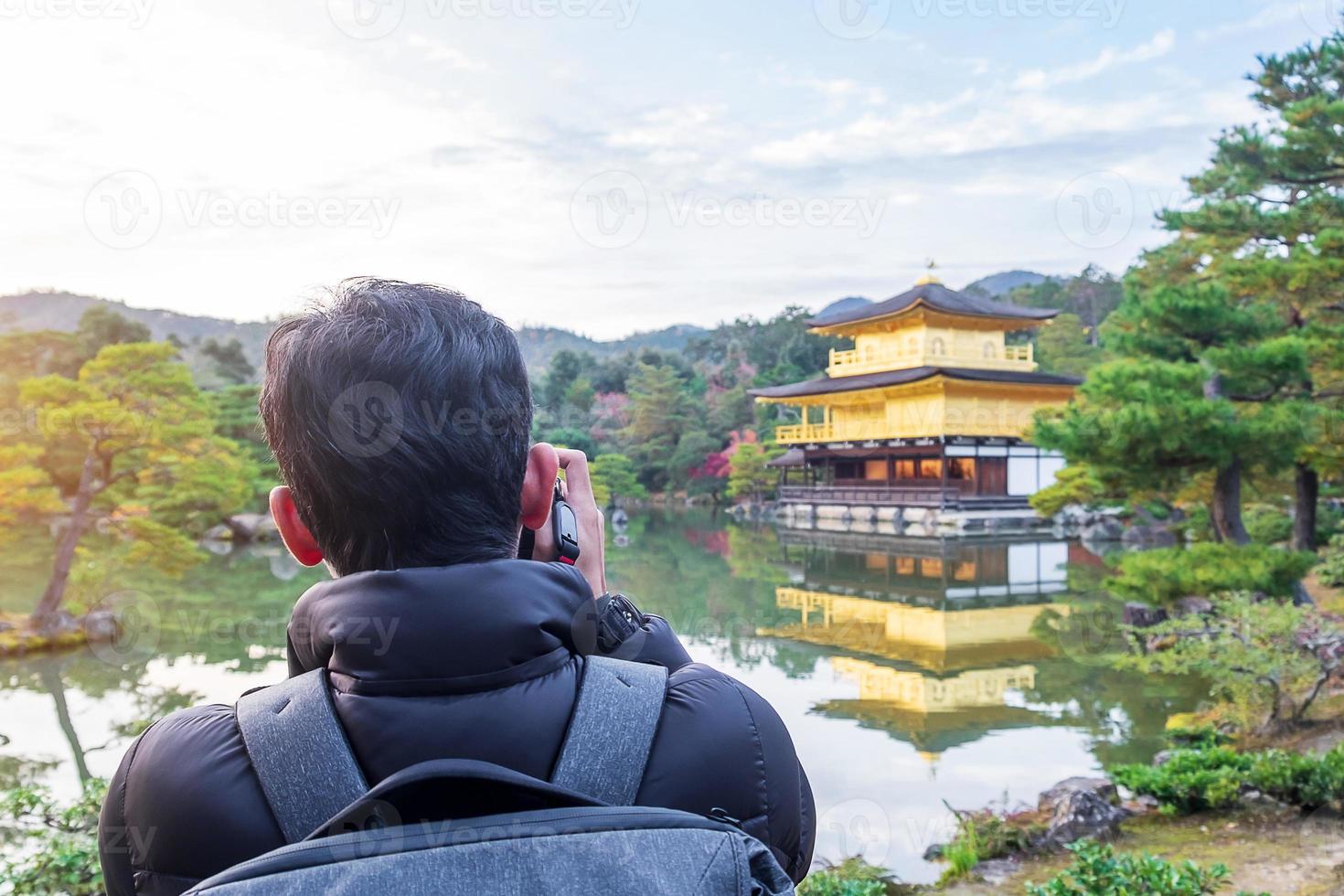 solo man tourist taking photo by camera at Kinkakuji temple or the golden pavilion in Autumn season, Asian traveler visit in Kyoto, Japan. Vacation, destination and travel concept