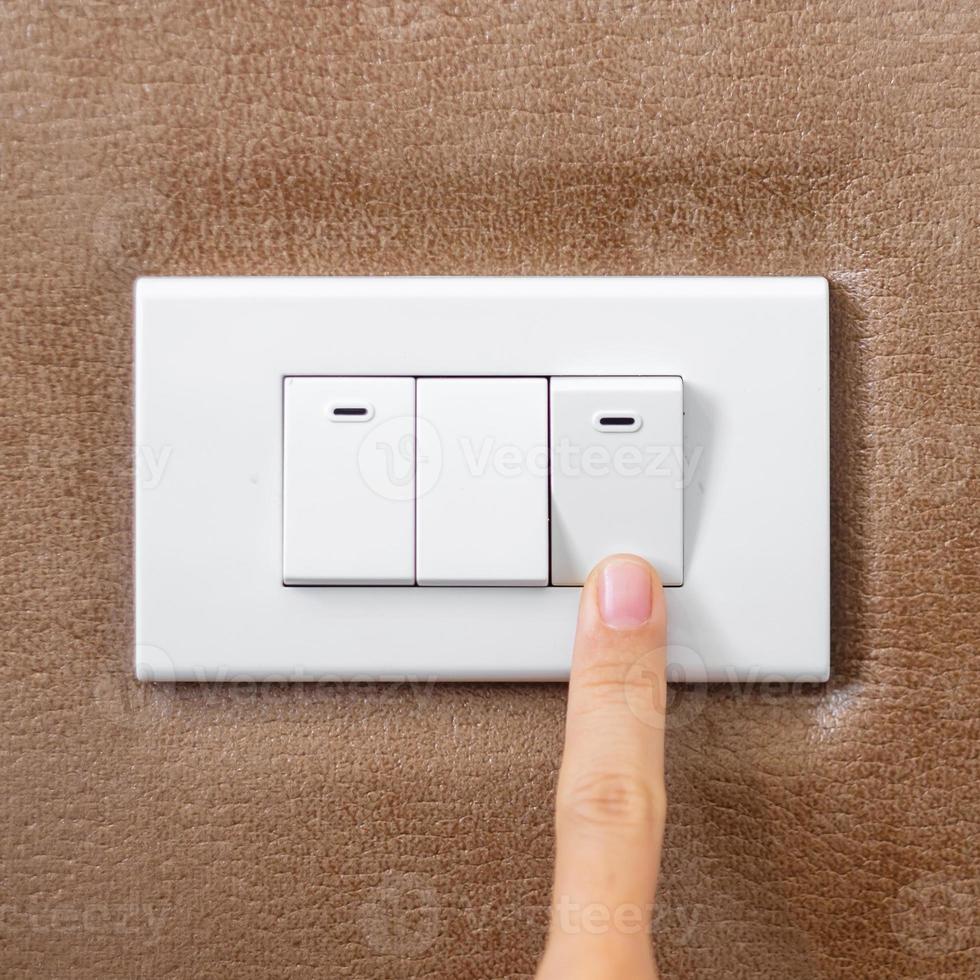 dedo encienda o apague el interruptor de luz en la pared en casa. conceptos de ahorro de energía, energía, electricidad y estilo de vida foto