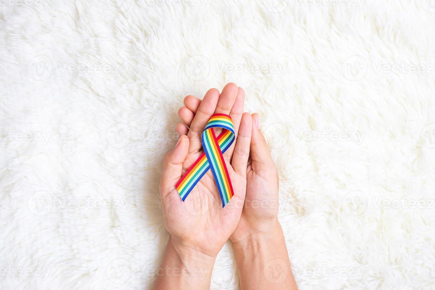 hand showing LGBTQ Rainbow ribbon on white bed background. Support Lesbian, Gay, Bisexual, Transgender, Queer community and Rights concept photo
