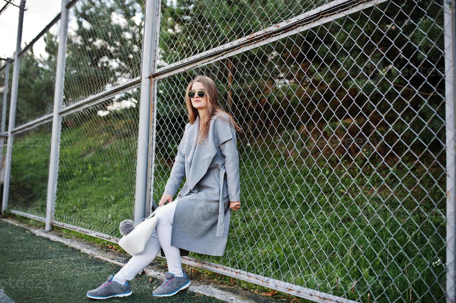 Girl in gray coat with sunglasses at small street stadium. photo