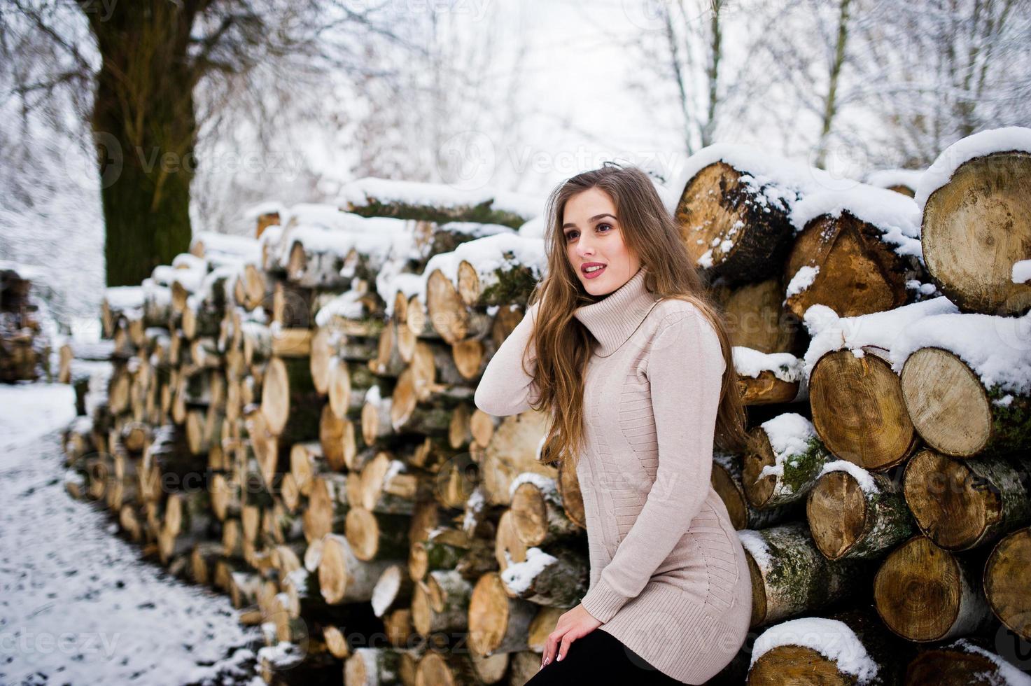 Beautiful brunette girl in winter warm clothing. Model on winter sweater near stump. photo