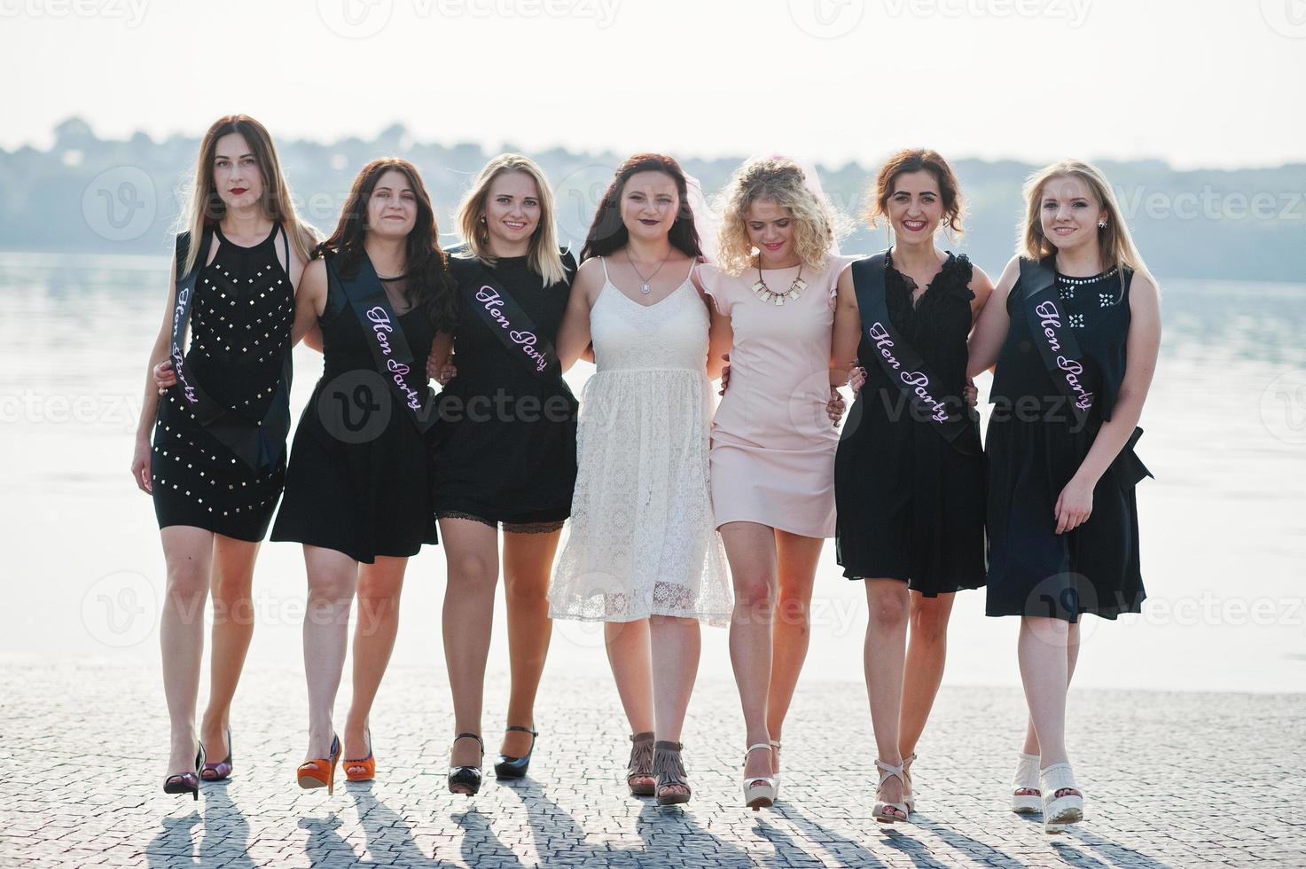 Group of 7 girls wear on black and 2 brides at hen party against sunny beach. photo
