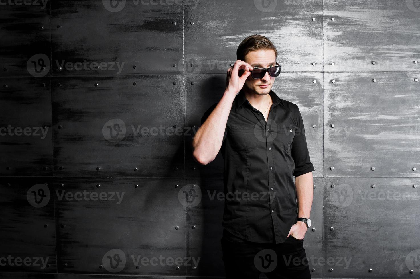 retrato de estudio de hombre elegante vestido con camisa negra y gafas contra la pared de acero. foto