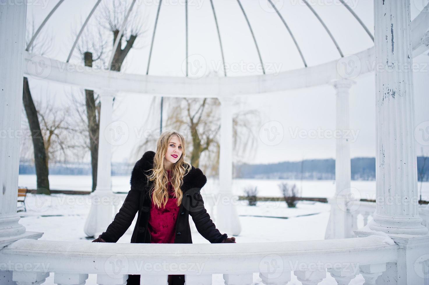 Elegance blonde girl in fur coat and red evening dress posed at winter snowy day. photo