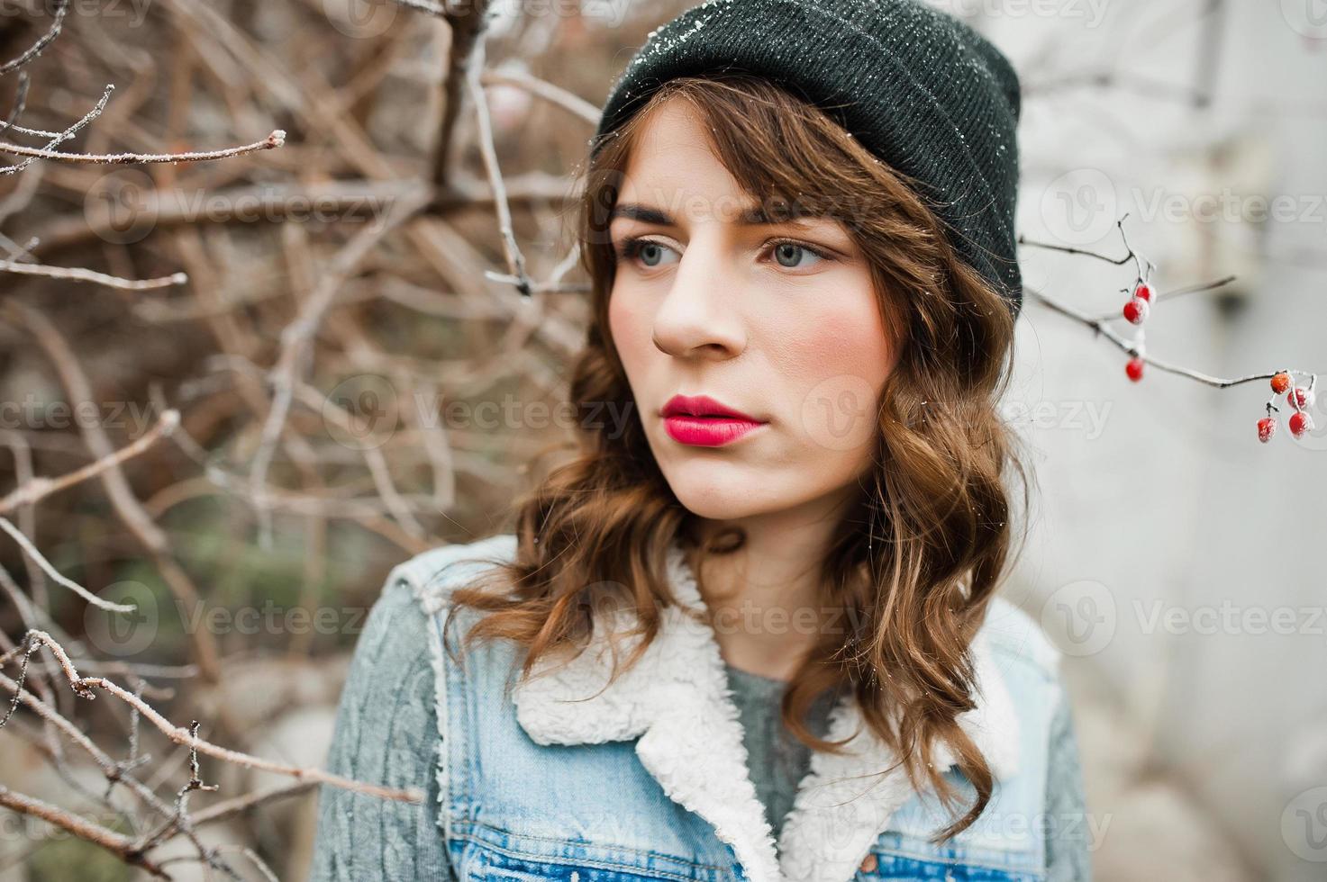 Portrait of brunette girl in hat  and jeans jacket at frozen bushes. photo