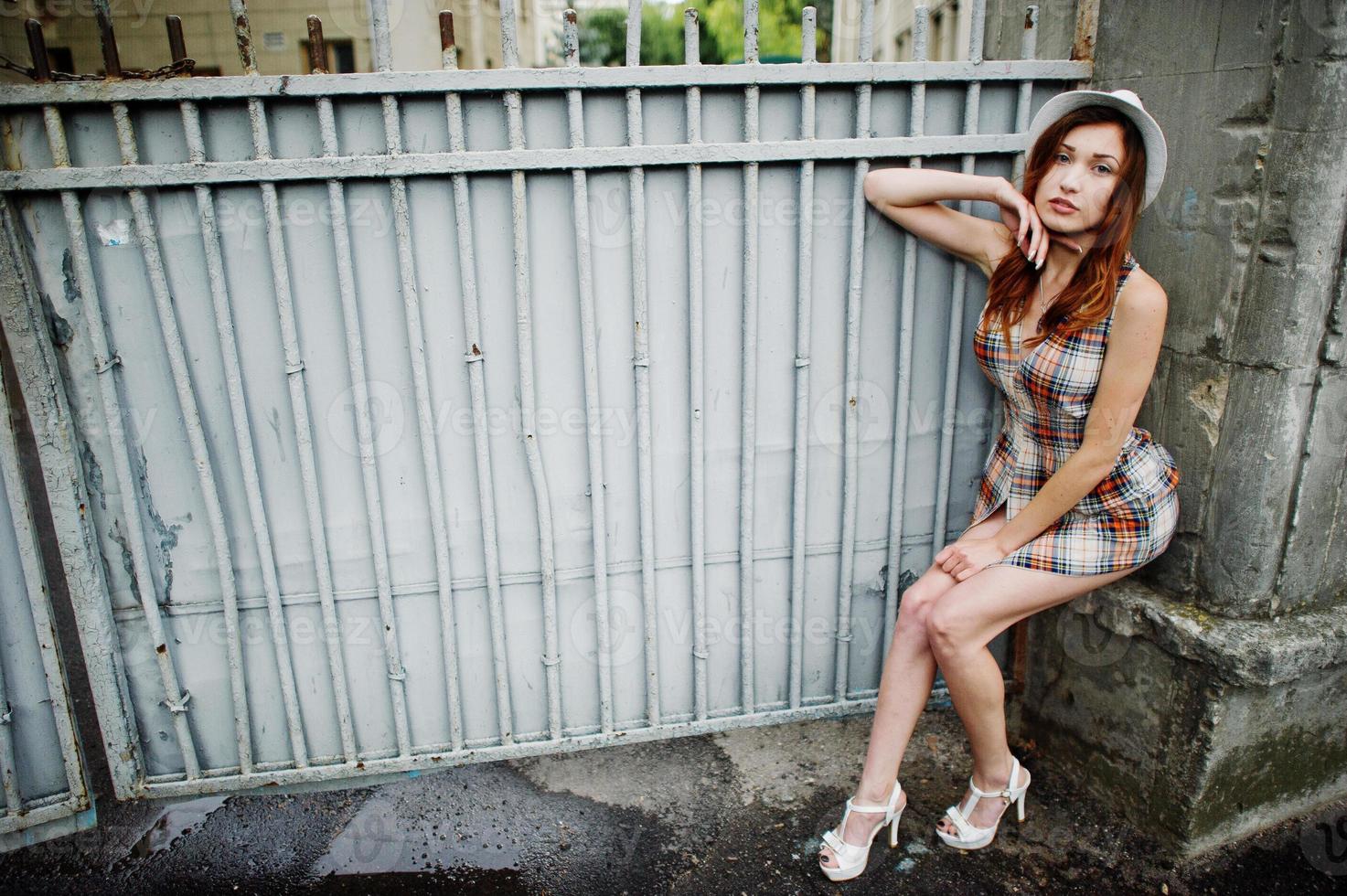 Amazing long legs with hig heels girl wear on hat against iron fence. photo