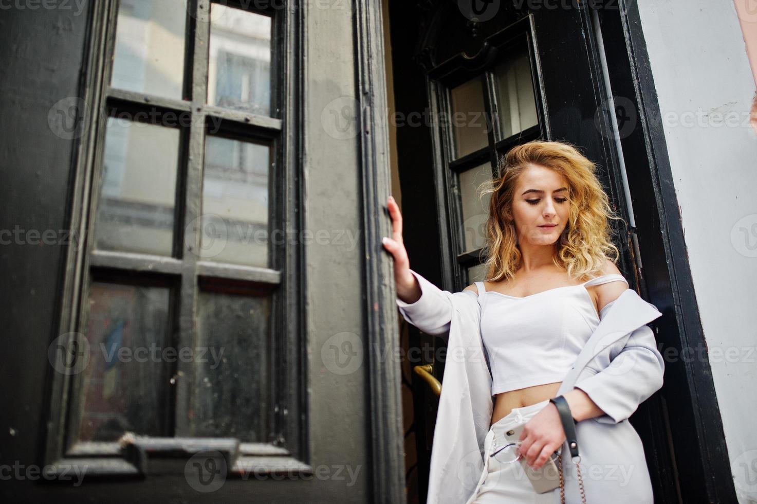 Stylish curly blonde model girl wear on white posing against old wooden door. photo