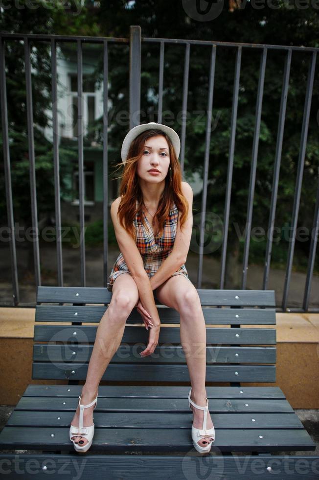 Amazing long legs with hig heels girl wear on hat posing at bench. photo